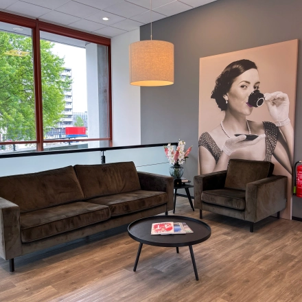 Stylish office lounge with a large window at Daalwijkdreef 47, Amsterdam Duivendrecht, perfect for office space rental. Features a cozy seating area with modern furniture and decorative art on the wall.
