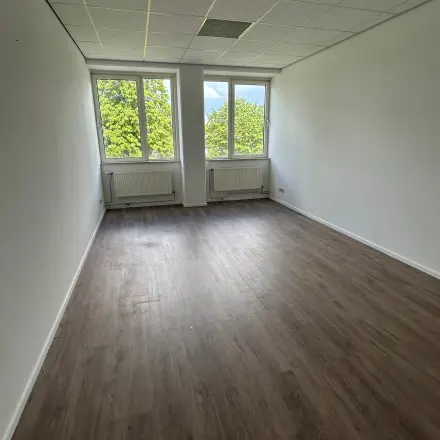 Empty office space at James Wattstraat 71, Amsterdam East, featuring large windows providing natural light and wooden flooring, ideal for office space rental.