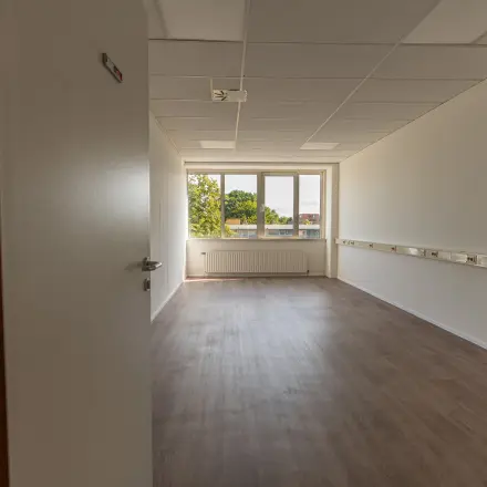 Unfurnished office space available for rent at James Wattstraat 71, Amsterdam East, featuring a bright room with wooden flooring and a large window.