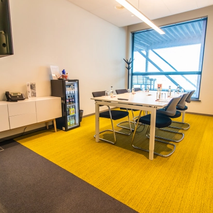 Office space rental at Piet Heinkade 55 in Amsterdam East featuring a modern conference room with a large table and chairs, bright yellow carpet, and a window view.