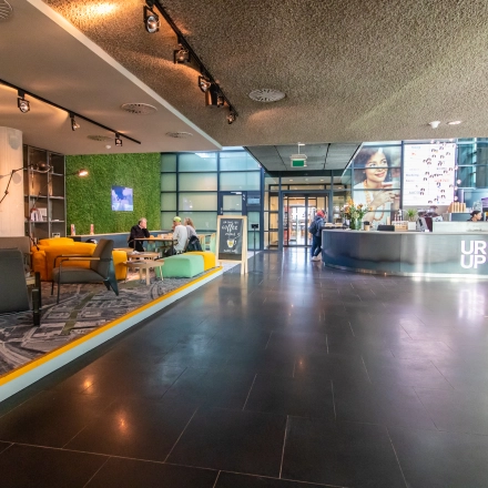 Spacious office lobby at Piet Heinkade 55, Amsterdam East, featuring modern furnishings and people engaging in business conversations, ideal for office space rental.