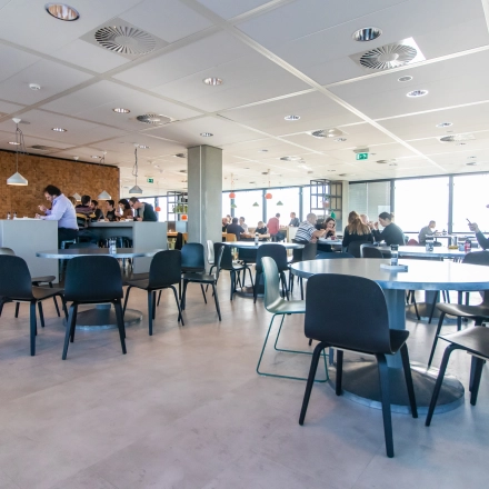 Modern office space in Amsterdam East at Piet Heinkade 55 with professionals engaged in work discussions at tables, highlighting a bright and collaborative environment ideal for office space rental.