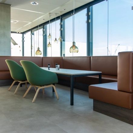 Modern office lounge area with large windows, green chairs, and brown leather seating at Piet Heinkade 55, ideal for an office space rental in Amsterdam East.