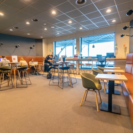 Modern office space rental at Piet Heinkade 55 in Amsterdam East, featuring stylish furniture and individuals engaged in meetings and work discussions.