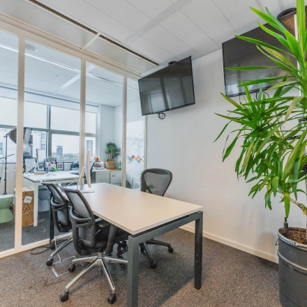 Furnished office space at Piet Heinkade 95B, Amsterdam East, featuring a conference table, chairs, a wall-mounted TV, and large windows for natural light. Ideal office space rental option.