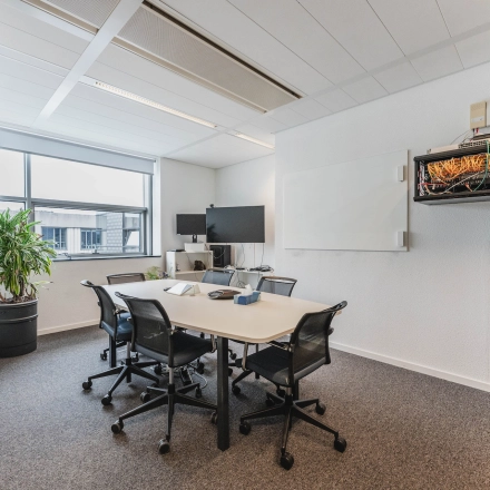 Modern office space at Piet Heinkade 95B, Amsterdam East, featuring a meeting table, chairs, and a large window with natural light. Ideal for office space rental.