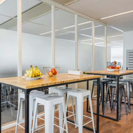 Modern office space at Piet Heinkade 95B, Amsterdam East, featuring high tables with stools, frosted glass walls, and trendy decor ideal for office space rental.