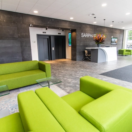 Bright and welcoming office space rental in Amsterdam East, featuring vibrant green sofas, a modern reception area, and elevators. Ideal for businesses looking to rent office space at Rhijnspoorplein 10-38.