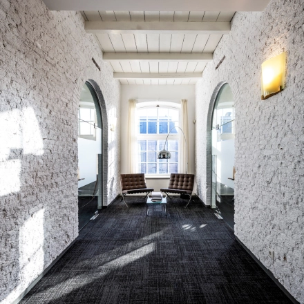 Bright office area at Sarphatistraat 370 in Amsterdam East with textured walls, seating, and natural light. Ideal office space rental location.
