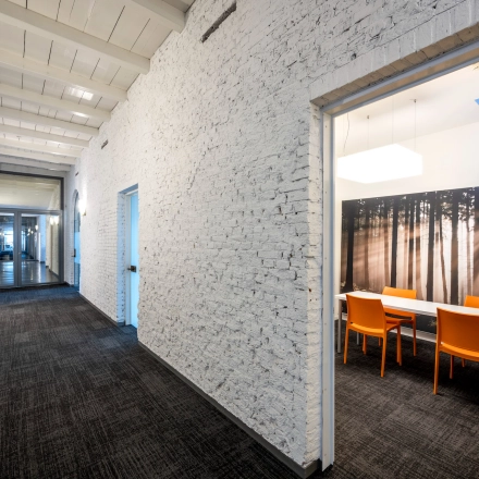 Interior hallway at Sarphatistraat 370, Amsterdam East, leading to a furnished office space with bright orange chairs and a forest-themed wall. Ideal office space rental with modern amenities.
