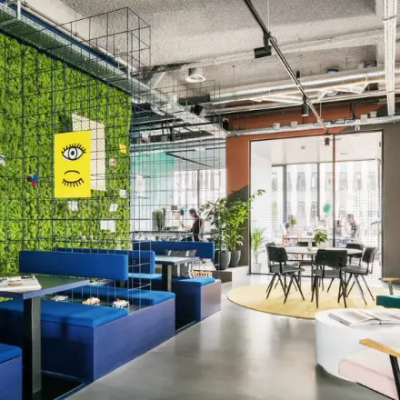 Modern office space at Jan van Galenstraat 335, Amsterdam New-West, featuring colorful furniture, a vibrant green wall, and open seating. Ideal for office space rental.