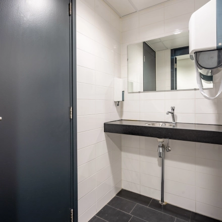 Modern restroom at an office for rent in Amsterdam New-West with a sleek black countertop and white tiled walls.