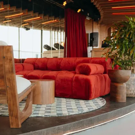 Stylish office lounge at Overhoeksplein 1, Amsterdam North with plush red sofa, wooden furnishings, and vibrant plants, ideal for office space rental.