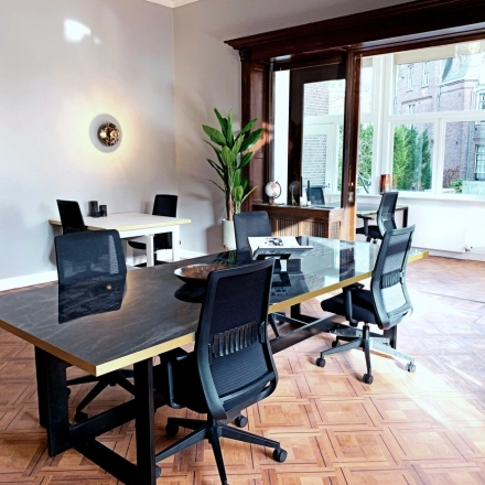 Bright office space in Amsterdam Old South at Emmalaan 7-9, featuring modern desks and chairs available for rent. Large windows allow natural light, ideal for productive work environments.
