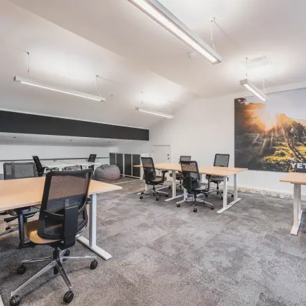 Modern office space with multiple desks and chairs, located in Olympisch Stadion, Amsterdam Old South, available for rent. Large wall art and ample lighting enhance the professional environment.