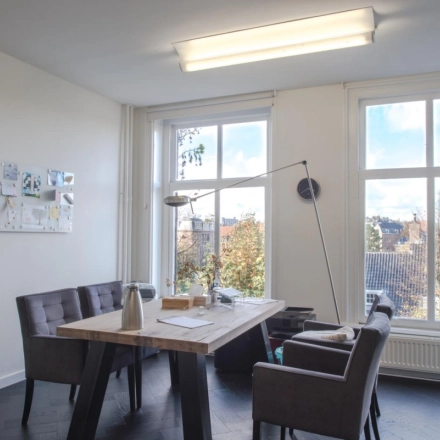 Furnished office space to rent at Sophialaan 21, Amsterdam Old South, featuring a wooden table with chairs and a view through large windows.