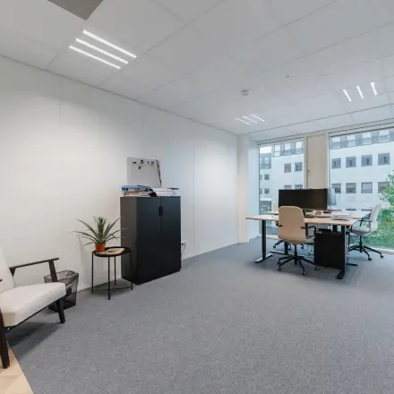 Furnished office space at John M. Keynesplein 4-10, Amsterdam Riekerpolder, featuring a desk, chairs, and cabinets near a large window with city views.
