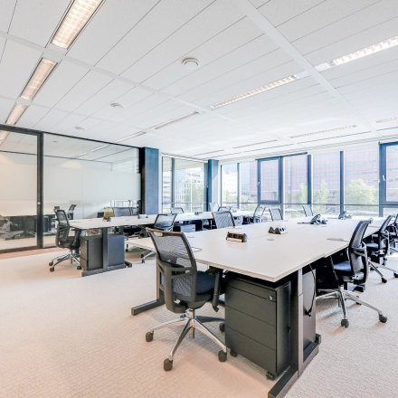 Bright office space for rent in Amsterdam Riekerpolder with desks, chairs, and large windows offering city views.