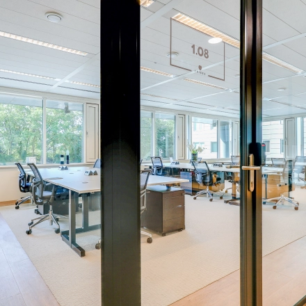 Spacious office space to rent in Amsterdam Riekerpolder, featuring large windows, multiple desks, and ergonomic chairs, offering a bright and professional workspace.