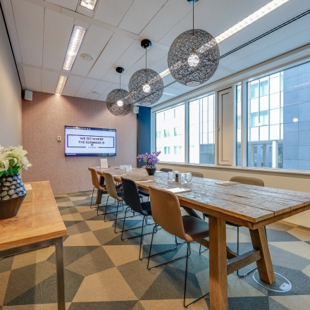 A stylish conference room at Thomas R. Malthusstraat 1-3 in Amsterdam Riekerpolder, featuring a long wooden table, chairs, and pendant lighting, perfect for office space rental.