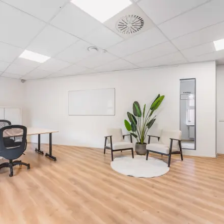 Bright office space with wooden flooring, two modern chairs, a desk with an office chair, and a potted plant. Ideal for office space rental in Amsterdam Sloterdijk.