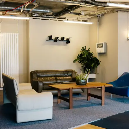 Interior view of a furnished office lounge at Kabelweg 24, Amsterdam Sloterdijk, featuring modern seating and a coffee table. Ideal for office space rental.