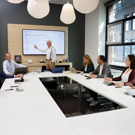 A team engaged in a meeting around a modern conference room table at Teleportboulevard 110, with large windows providing natural light in Amsterdam Sloterdijk. A perfect office space rental opportunity.