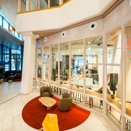 Inviting and modern lobby area with a view into an open office space. Comfortable seating and glass walls enhance the sense of openness, ideal for a collaborative office space rental.