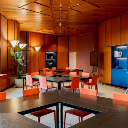 Modern office space with wood paneling, vibrant orange chairs around tables, and large screens, ideal for office space rental in Amsterdam South East.