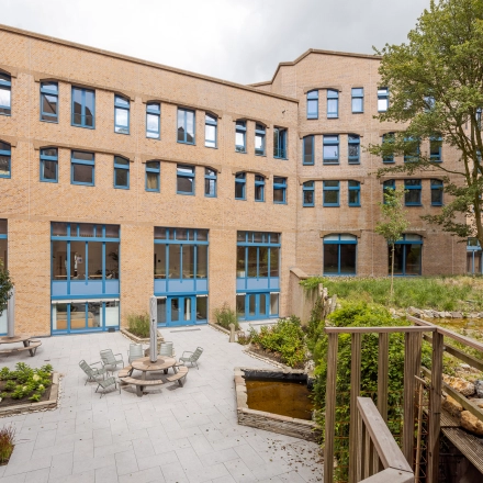 Exterior view of Bijlmerplein 888 in Amsterdam South East, showcasing a brick building and a peaceful patio. Ideal office space rental with outdoor seating options.