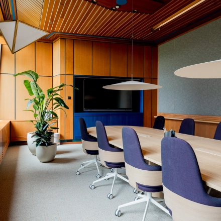 Elegant office space featuring a long wooden table, blue chairs, a large TV, and potted plant at Bijlmerplein 888, ideal for office space rental in Amsterdam South East.