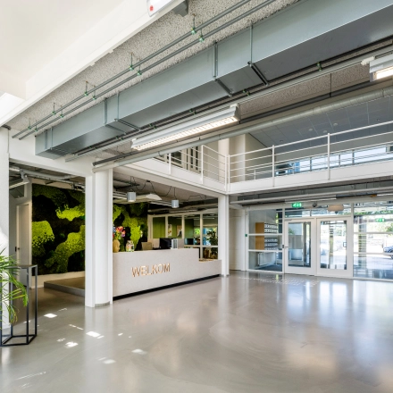 Spacious entrance area of an office to rent at Burgemeester Stramanweg 102, Amsterdam South East, featuring a modern reception desk and greenery for office space rental.
