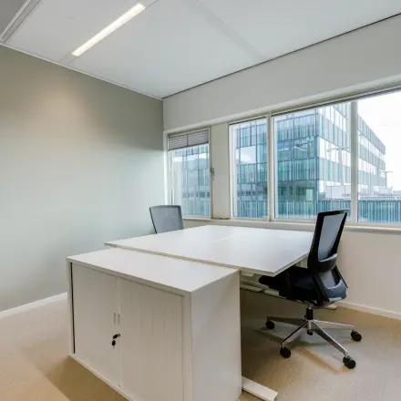 Furnished office space rental at Herikerbergweg 288, Amsterdam South East, featuring two modern desks with chairs and large windows overlooking the city.