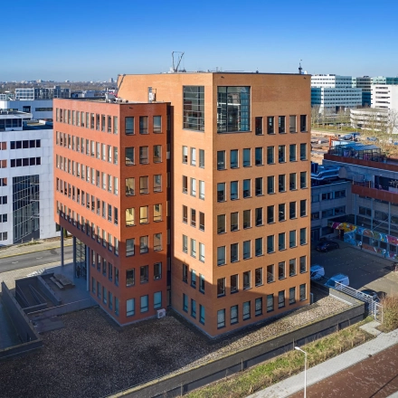 Exterior view of Hogehilweg 24, featuring an office building in Amsterdam South East with red and white facades. Ideal for those seeking office space rental opportunities.