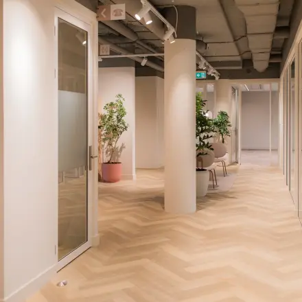Interior view of a modern office space at Hullenbergweg 109-135, Amsterdam South East, showcasing a clean corridor with glass doors and potted plants, available for office space rental.
