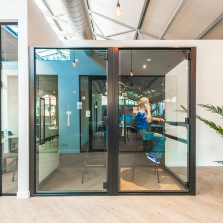 Modern office space at Luttenbergweg 8, Amsterdam South East with glass partitions and a person engaged in business activities, ideal for office space rental.