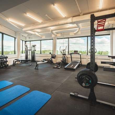 A well-equipped fitness room with exercise machines, weights, and blue mats at Luttenbergweg 8. Ideal for tenants looking to complement their office space rental with workout facilities in Amsterdam South East.