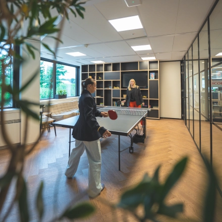 Two people playing table tennis in a well-lit office with wooden floors and large windows at Luttenbergweg 8, Amsterdam South East. Ideal for office space rental.