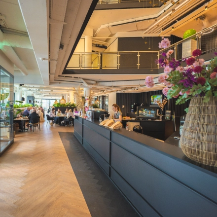 Modern office space for rent at Luttenbergweg 8, Amsterdam South East, featuring a stylish reception with people engaged in business discussions.