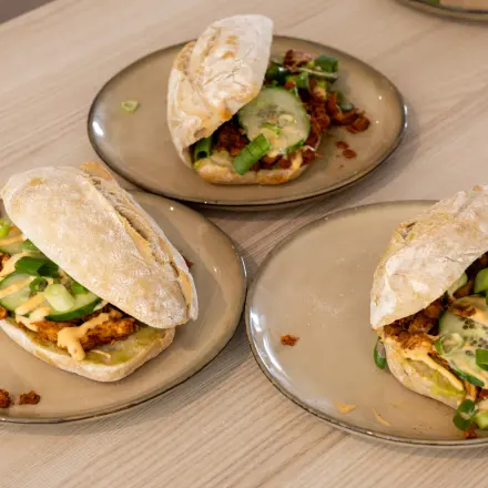 Three plates with sandwiches featuring a variety of toppings on a wooden table.