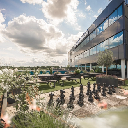Modern office to rent at Luttenbergweg 8, Amsterdam South East, featuring an outdoor area with picnic tables and a large chessboard set against a reflective building facade.
