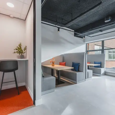 Modern office space at Paasheuvelweg 20, Amsterdam South East, with various seating options available for rent, including cozy booths and a high stool. Bright and inviting area for office space rental.