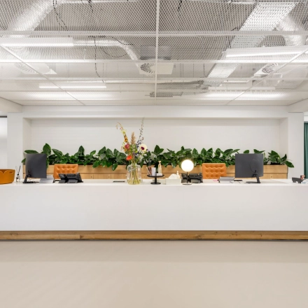 Spacious office in Amsterdam West with a modern, furnished reception area featuring a large desk and green accents. Ideal for office space rental.