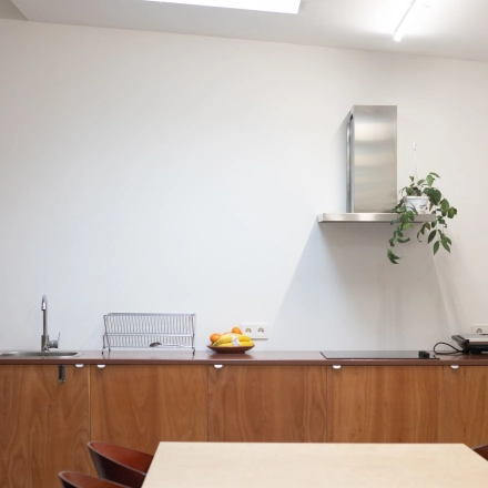 Modern, minimalistic kitchen space in an office to rent at Hondiusstraat 7H, Amsterdam West. Features a sleek counter, wooden cabinets, and a skylight for natural light.