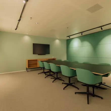 Modern conference room with a large table, green chairs, and a wall-mounted screen, ideal for office space rental at Kon. Wilhelminaplein 4 in Amsterdam West.