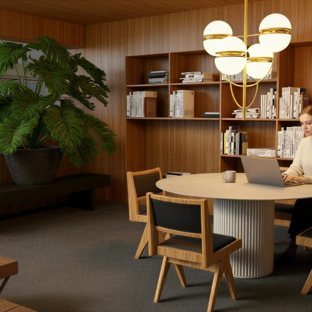 A furnished office at Barbara Strozzilaan 101, Amsterdam Zuidas, features wooden decor, bookshelves, a round table, and a person working on a laptop. Ideal for office space rental.