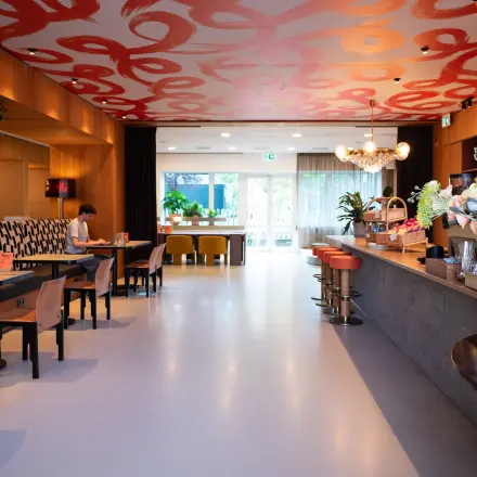 Modern office workspace at Barbara Strozzilaan 101, Amsterdam Zuidas, featuring a stylish interior with tables, chairs, and vibrant artwork. People are engaged in business activities. Ideal for office space rental.