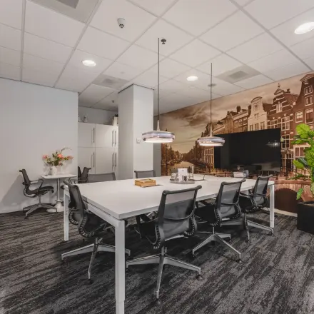 Modern conference room in Claude Debussylaan 10, Amsterdam Zuidas, featuring a large table, office chairs, and wall art of Dutch canal houses. Perfect office space rental opportunity.