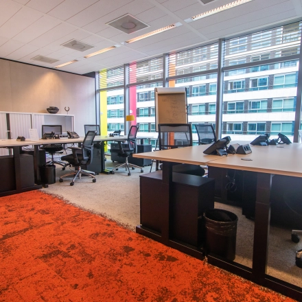 Modern office space with large windows and multiple workstations available for rent at Claude Debussylaan 7-29, Amsterdam Zuidas. The bright interior features desks and chairs, ideal for office space rental.
