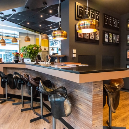 A stylish workspace at Claude Debussylaan 7-29, Amsterdam Zuidas, featuring a bar-style table with saddle stools, plants, and decorative lighting, ideal for office space rental.